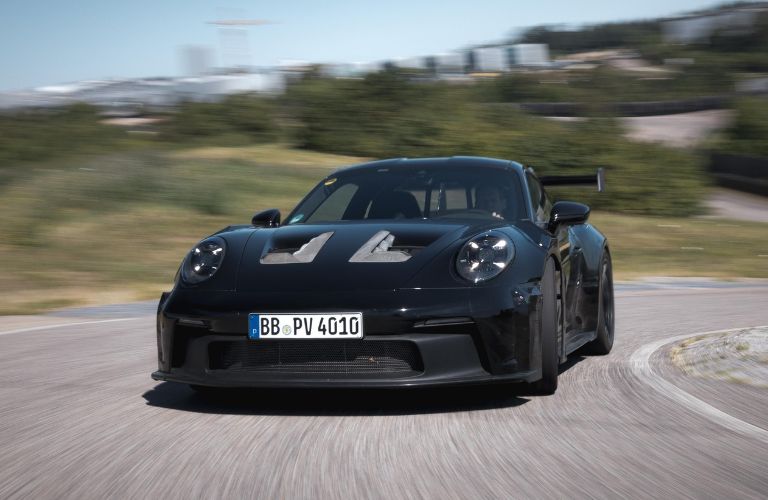 Front view of a black 2023 Porsche 911 GT3 RS driving on a road