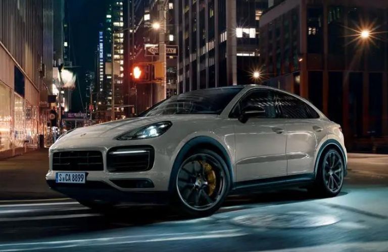 Side view of a silver 2022 Porsche Cayenne driving on a road at night.
