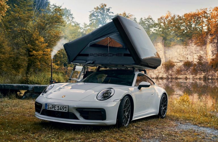 Front view of a white Porsche 911 with the roof tent installed parked at a campsite in the woods.